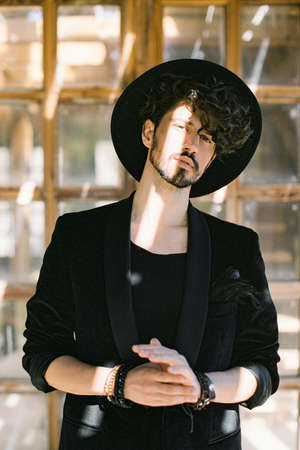 Portrait of a young man in a black hat on the background of a wooden window