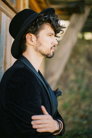 Profile of a young man in a hat standing near the wall of the house