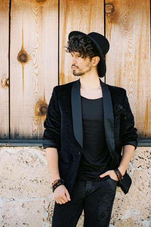 Man in a black hat against a wooden wall