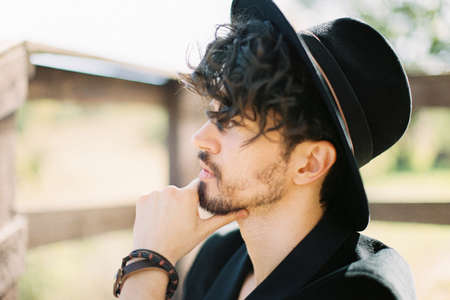 Man in a black hat touches his chin with his fingers. Portrait