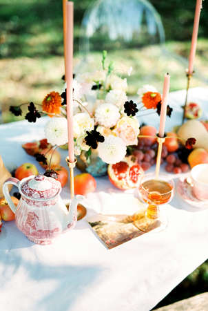 Bouquet of flowers next to fruits and candles stands on a table in the gardenの写真素材