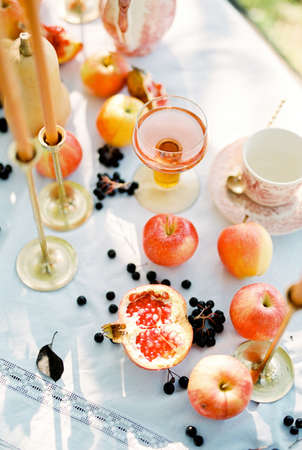Pomegranates and apples lie on a white tablecloth on a table next to candlesの写真素材