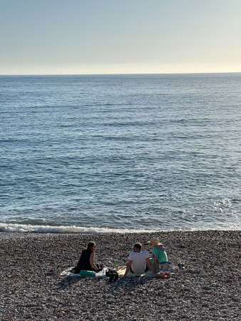 Three people sit on a blanket on a pebble beach by the seaの写真素材
