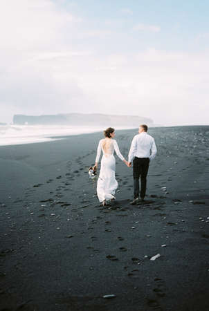 Bride and groom walk on the black sand. Vik Beach, Icelandの写真素材