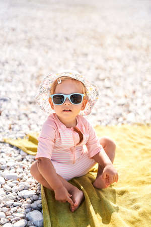 Little girl in sunglasses and panama sits on the beachの写真素材