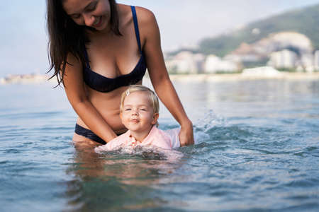 Little girl swims with her tongue out, supported by her motherの写真素材