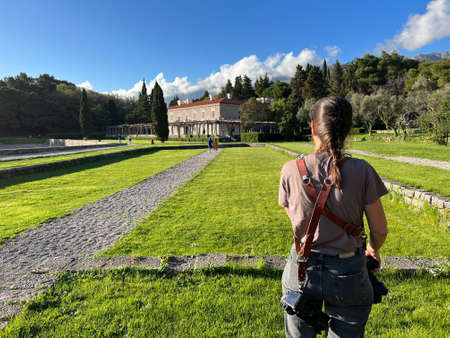 Girl photographer stands in the garden of Villa Milocer. Back view