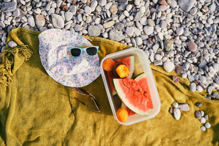 Plastic box with watermelon and peaches on a blanket on the beach