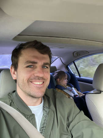 Dad carries a sleeping girl in a child seat in the back of the car