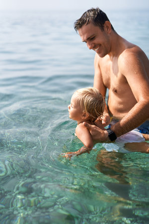 Smiling dad teaches little daughter to swim holding her hands under armpitsの写真素材