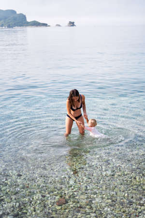 Mom teaches little girl to swim holding her handsの写真素材