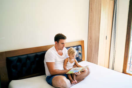 Dad reads a book to a little girl on the bed