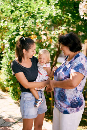 Mom holds a little girl in her arms next to a standing grandmother
