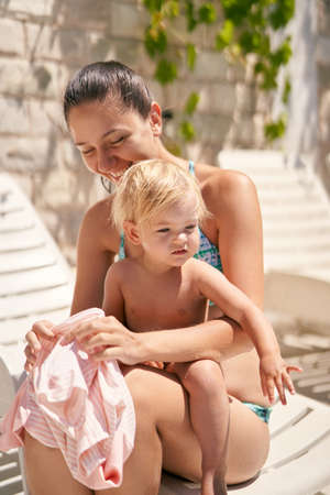 Mother putting on a t-shirt on a small baby sitting on her lapの写真素材