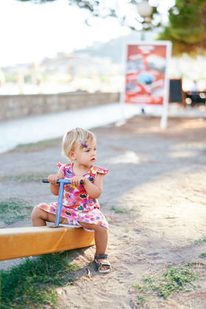 Little girl sits on the teeter-totter in the playgroundの写真素材