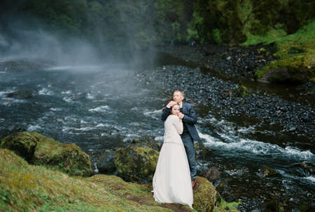 Groom hugs bride on the green bank of the river. Icelandの写真素材