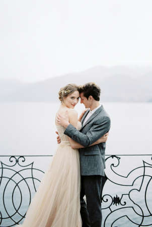 Bride and groom hug near the forged fence on the shoreの写真素材