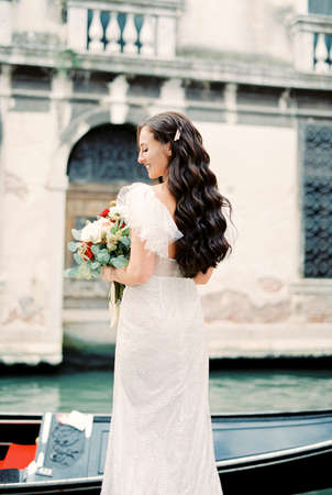 Bride with a bouquet stands on the bank of the canal in Venice. Back viewの写真素材