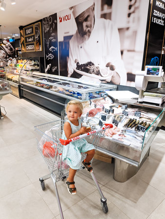 Budva, Montenegro - 12.07.22: Little girl sits in a cart near the counter with fish in a supermarketのeditorial素材
