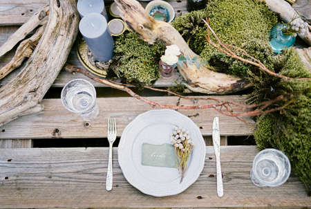 Bouquet of dried flowers on a plate near the candles and glasses on the table. Top view