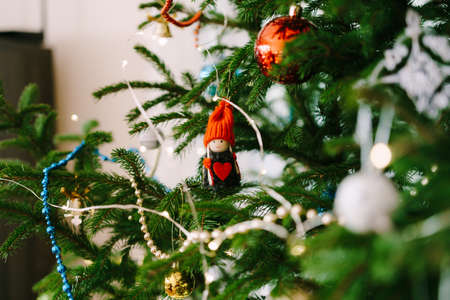 A Christmas tree toy on the branches of a tree - a little girl in a red hat with a big red heart.