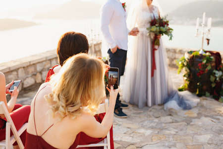 Guests at the wedding ceremony filming the bride and groom on the phonesの写真素材