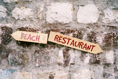 Two multidirectional signs with inscriptions hang on a stone wall. Title: Beach Restauranttの写真素材