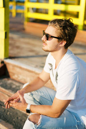 Young man in sunglasses sitting on the wooden stepsの写真素材