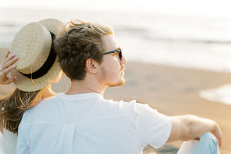 Woman sits on the sand leaning against a man
