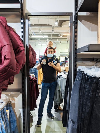 Budva, Montenegro - 07.07.22: Dad with a little girl on his shoulders is photographed in a mirror in a clothing storeのeditorial素材