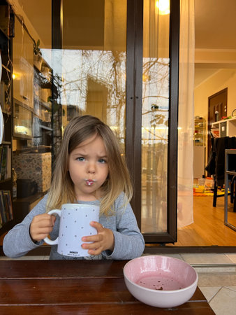 Budva, Montenegro - 06.07.22: Little girl drinks milk from a huge cup on the balconyのeditorial素材
