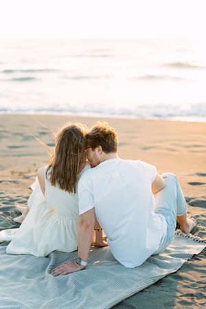 Man kissing woman shoulder while sitting on the beachの写真素材