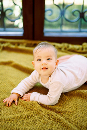 Baby lies on his tummy on a blanket on the floor