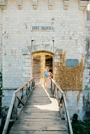 Groom hugs bride leaning against the railing of the wooden bridge to Mamula Fortの写真素材