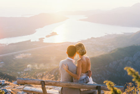 Bride sits on groom lap on a bench on the mountain. Back viewの写真素材