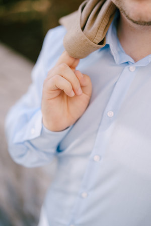 Groom in a blue shirt holds a brown jacket on his shoulder