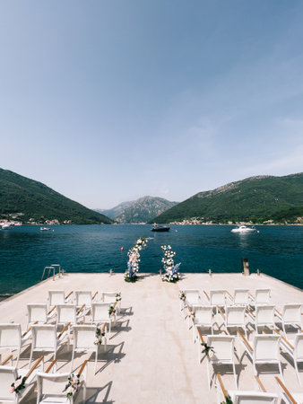 Rows of chairs decorated with flowers stand on the pier near the wedding semi-archの写真素材