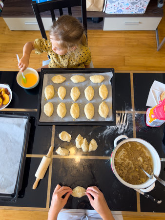 Mom makes stuffed buns that a little girl brushes with a beaten egg