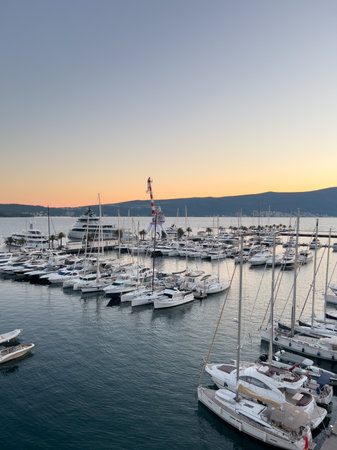 Crane stands on a pier among moored yachts against the backdrop of mountains at sunset