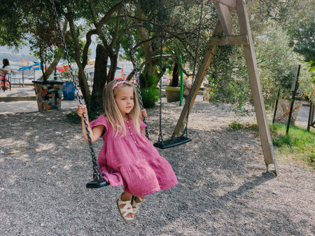 Little girl swings on a chain swing in the park among the treesの写真素材