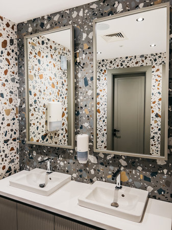 Wash basins with chrome faucets in a hotel bathroom with multi-colored tiles on the walls