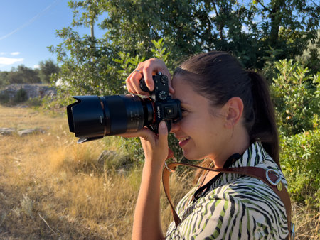 Girl photographer takes pictures with a digital camera with a retractable lens in the park