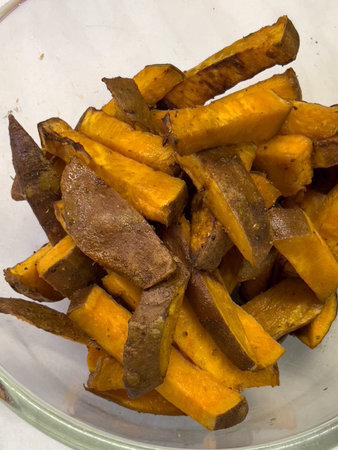 Pieces of baked crispy sweet potato lie in a deep glass bowl