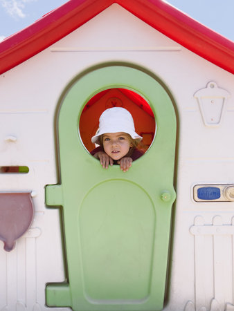 Little girl looks out the window on the door of a toy houseの写真素材