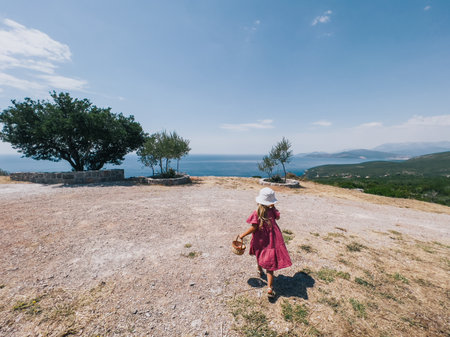 Little girl with a basket walks along a rocky hill towards the treesの写真素材