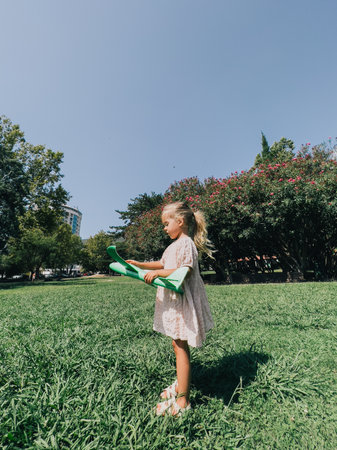 Little girl stands on a green lawn with a throwing glider in her handsの写真素材