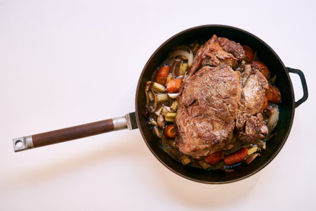 Frying pan with a wooden handle with roast beef and vegetables on a white table. Top viewの写真素材