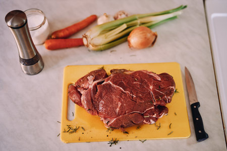 Piece of tenderloin sprinkled with rosemary lies on a cutting board on a table next to raw...