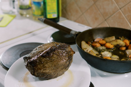 Baked tenderloin lies on a plate next to vegetables in a pan on the stoveの写真素材