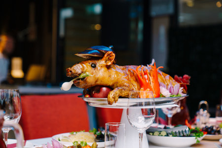 Roasted pig garnished with vegetables lies on a dish on a table in a restaurantの写真素材